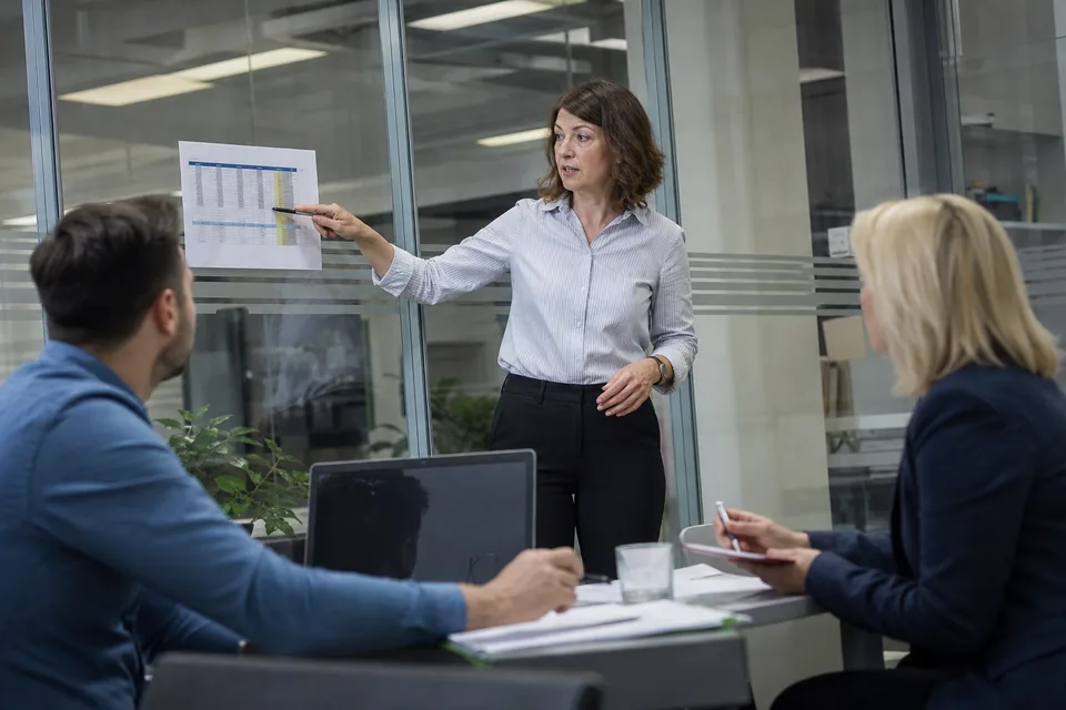 Kierowniczka finansów omawia z zespołem wydruk tabeli należności w sali spotkań